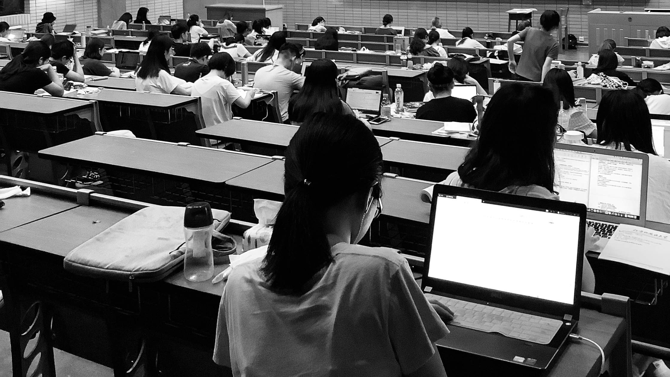 A grayscale image of people sitting in a lecture hall using laptops